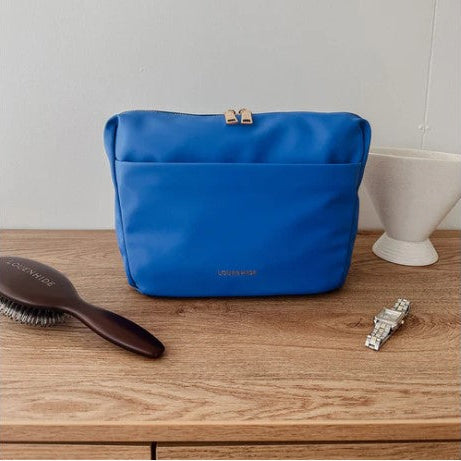 Blue toiletry bag on a wooden surface with a hairbrush and watch.