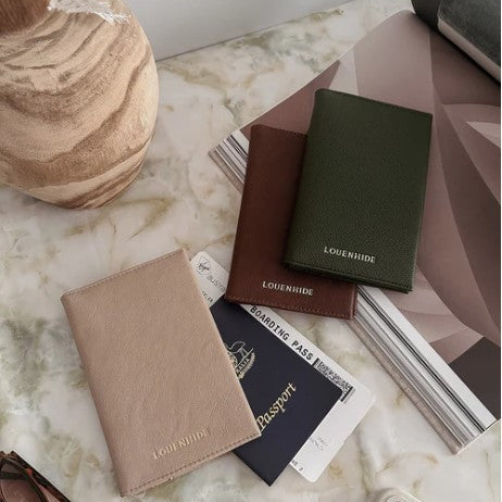 Three Louenheim leather wallets on a marble surface with a passport and boarding pass.