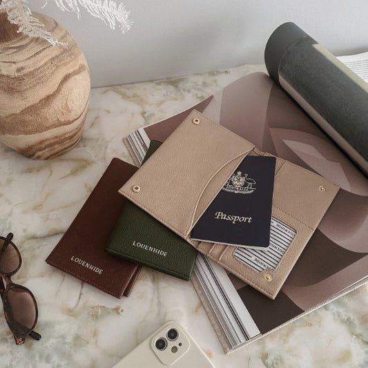 Collection of passport holders and a passport on a marble surface with sunglasses and a phone.