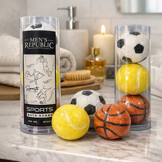 Men's Republic sports bath bombs displayed in clear cylindrical packaging on a marble bathroom counter, with soccer balls, tennis balls, and basketballs arranged around the tubes.