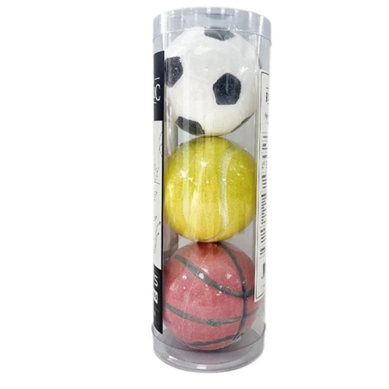 A set of three miniature sports balls bath bombs inside a clear plastic cylinder container, featuring a white soccer ball on top, a yellow tennis ball in the middle, and a red basketball on the bottom.