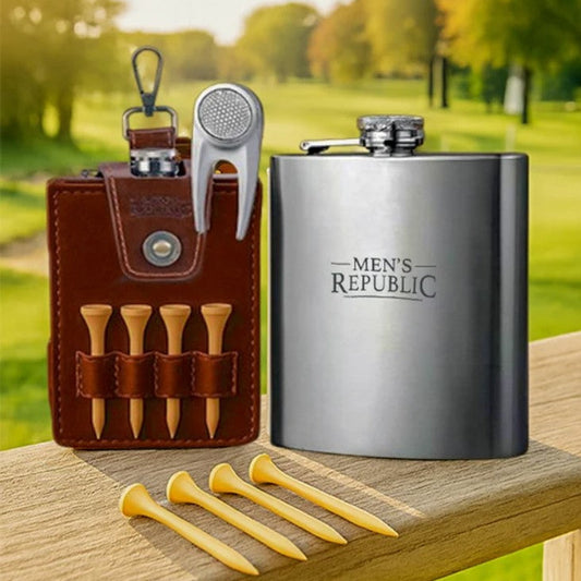 A men's golf accessory set displayed on a wooden railing with a blurred park background. The set includes a brown leather pouch with four wooden tees and a silver golf divot tool, a stainless steel flask engraved with 'MEN'S REPUBLIC', and four yellow tees in the foreground.