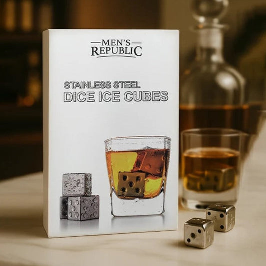 Men's Republic stainless steel dice ice cubes shown in their white retail box, with a whiskey glass, amber liquid, and metallic dice on a tabletop in a softly lit bar-like setting.
