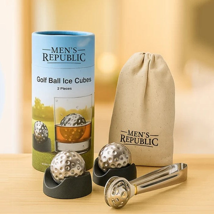 Men's Republic golf ball ice cubes set with two silver metal golf balls, a black holder, a metal tong, and a blue-and-green cylindrical package, alongside a beige drawstring pouch, on a wooden surface with a warm blurred background.
