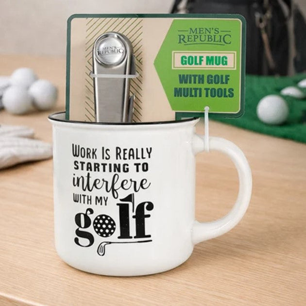 White ceramic golf mug with black text reading 'Work Is Really Starting To Interfere With My Golf' by Men's Republic, shown with a metal golf club head and green multi-tool package inserted into the mug on a wooden tabletop.