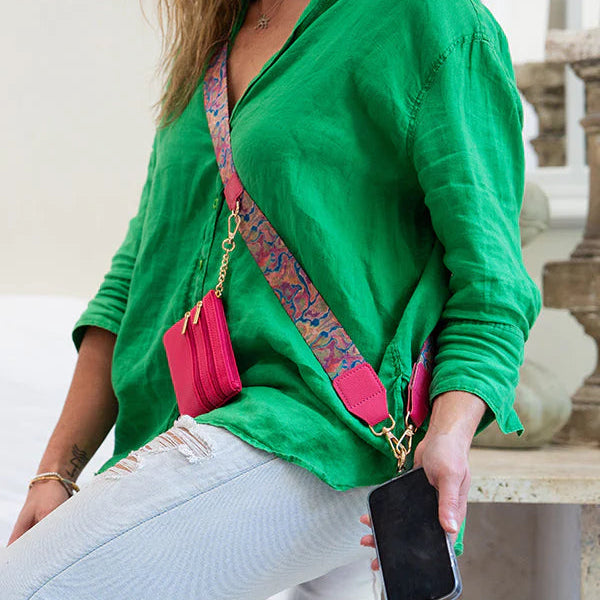 Person wearing a green shirt with a pink crossbody bag and holding a phone.