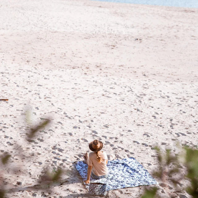Person sitting on a blanket on a sandy beach