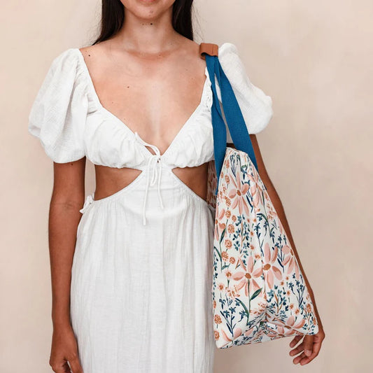 Woman in a white dress holding a floral bag against a beige background