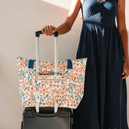 Person holding a floral-patterned tote bag over a suitcase against a plain background
