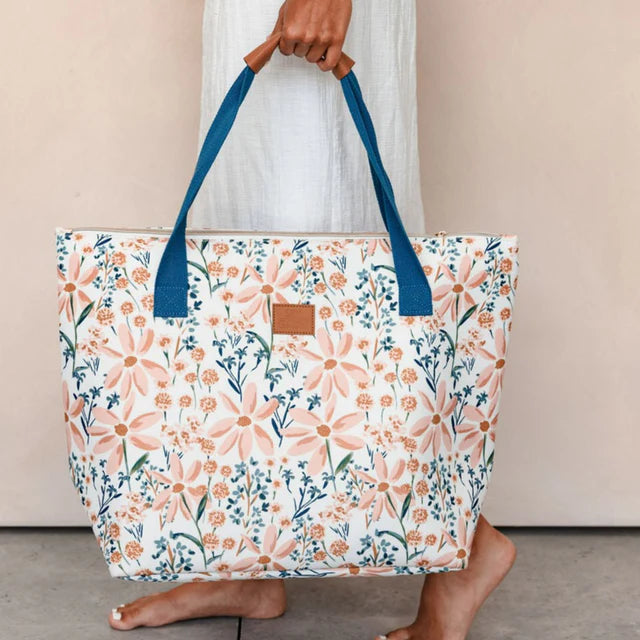 Floral tote bag with blue handles held by a person against a neutral background