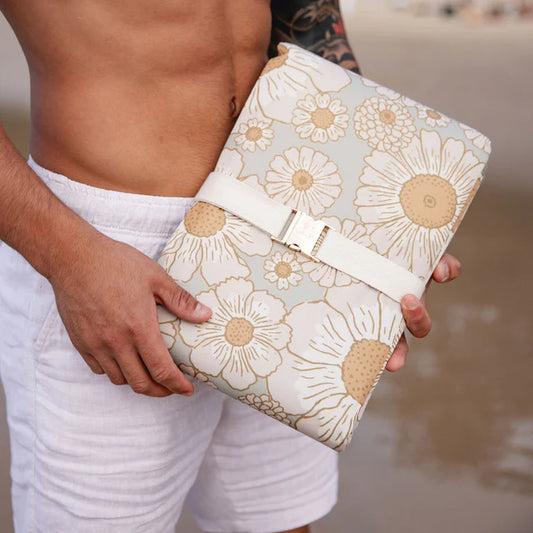 Person holding a floral picnic rug on a beach