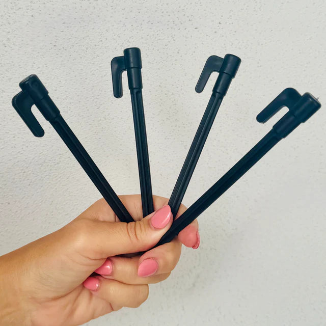 Hand holding four black pens with unique clips against a light gray background