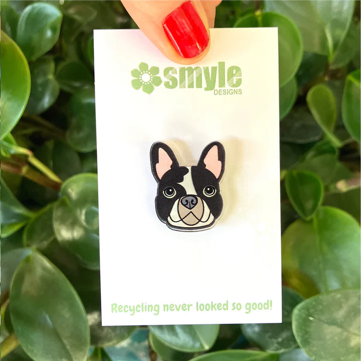 Pin with a dog design on a Smyle Designs card against a green leafy background