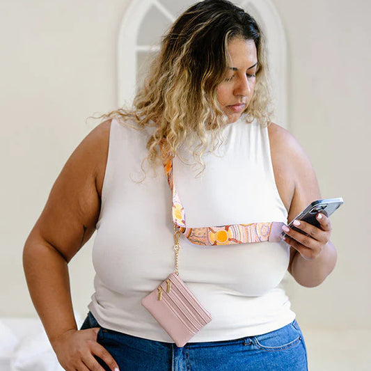 Woman using a smartphone with a pink wallet hanging from her shoulder.