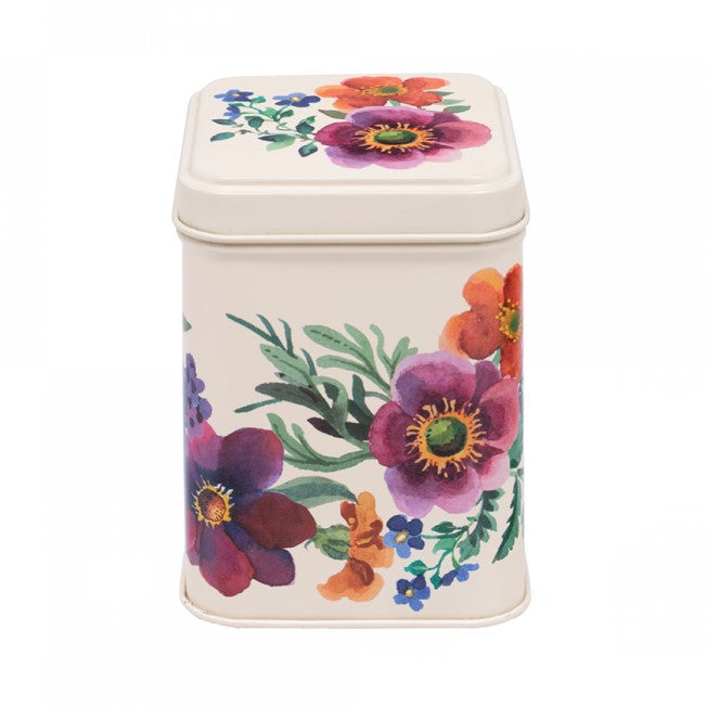 A square metal tea tin with a cream-colored body and lid, decorated with a vibrant watercolor floral pattern featuring purple, orange, and blue flowers with green leaves.